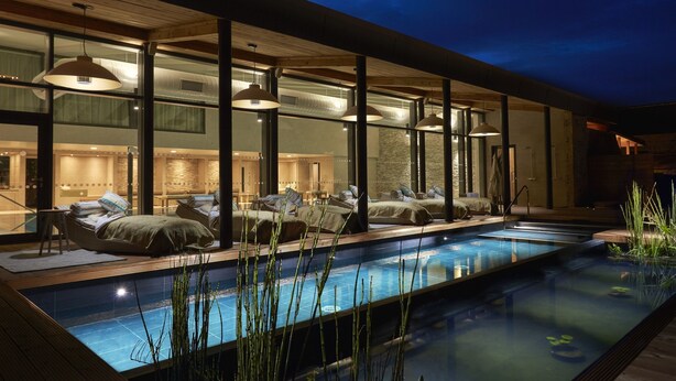 Un área de piscina exterior moderna con sillones de descanso y una terraza de madera.