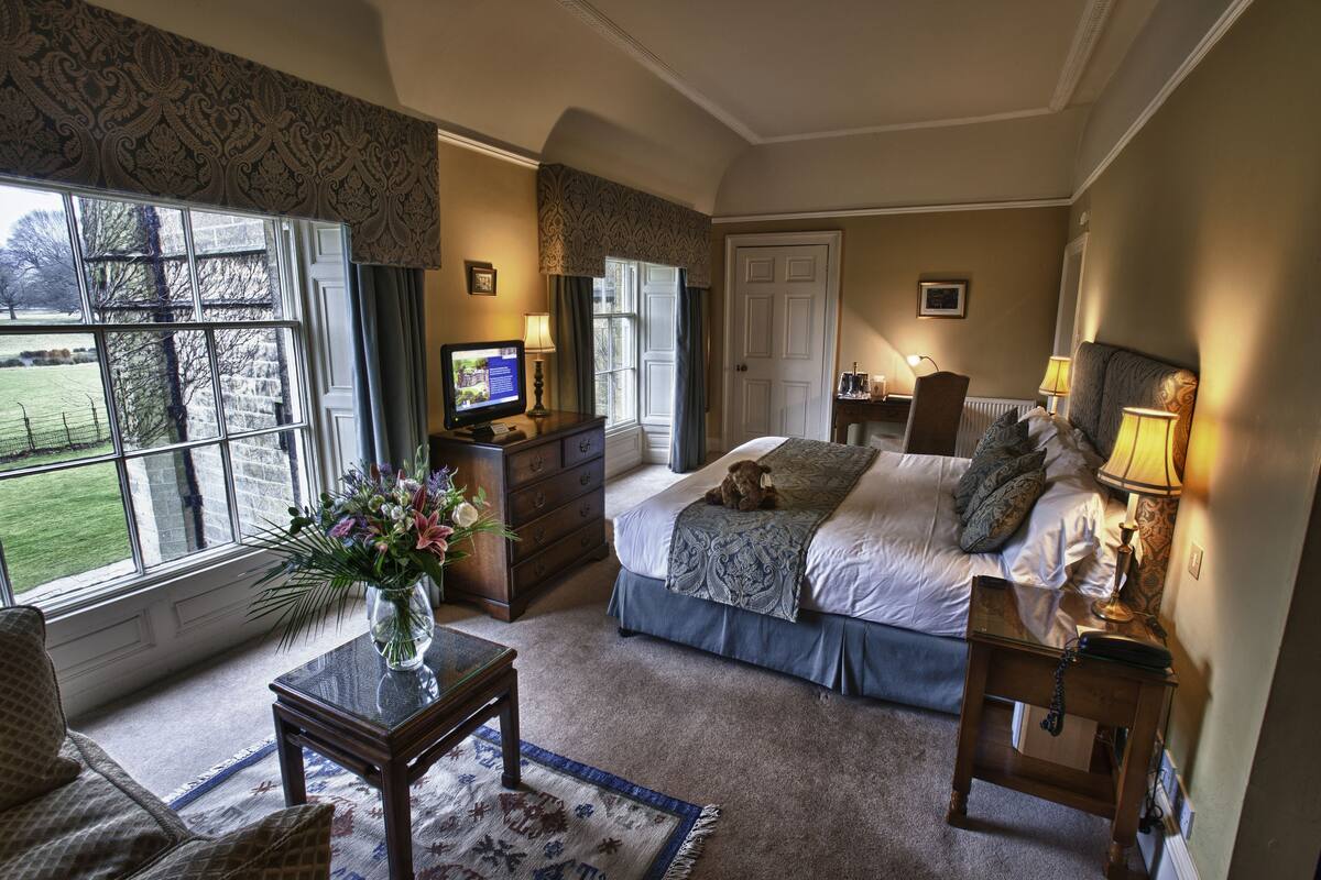 A bedroom with a bed, bedside table, lamp, dresser, and a television.
