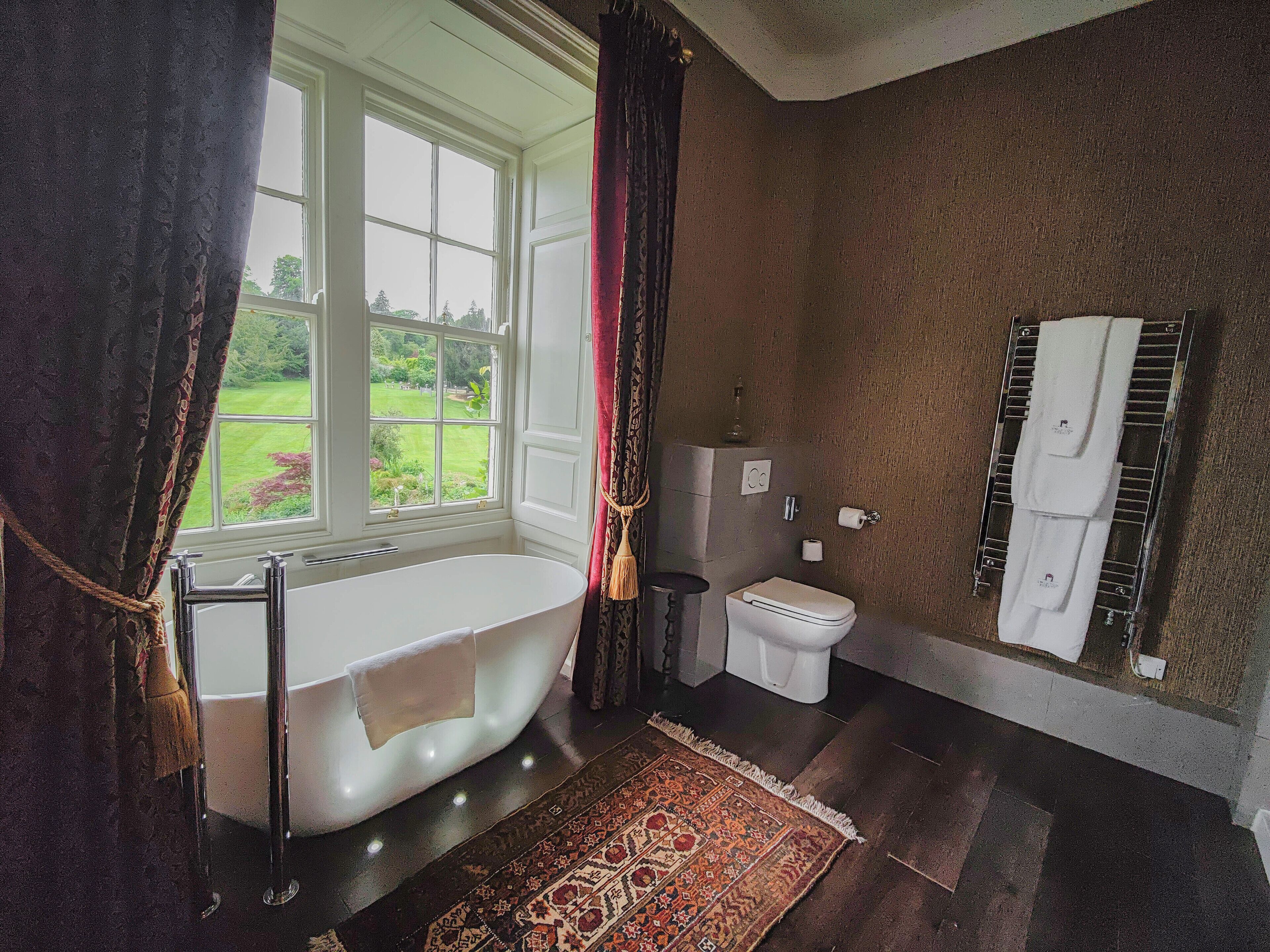 A bathroom with a bathtub, toilet, and a window with curtains.