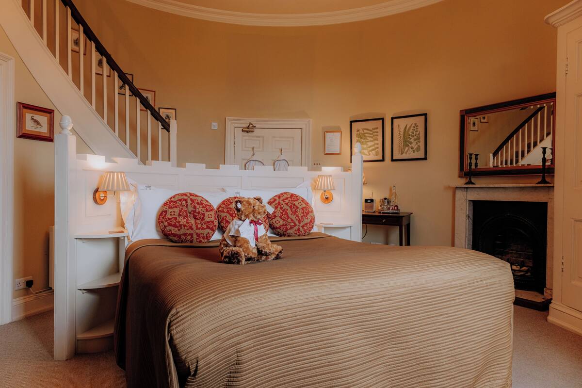 A bedroom with a large bed, a staircase, a fireplace, and wall-mounted lamps.