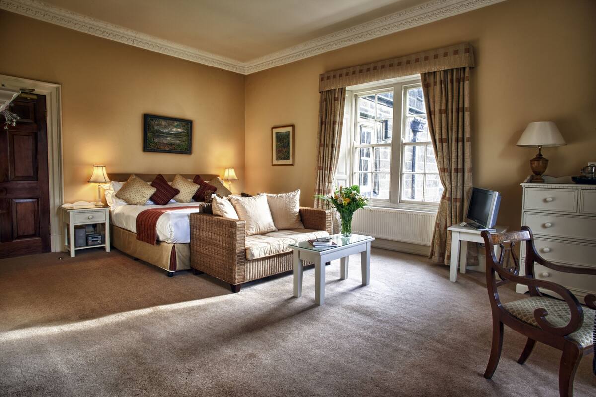 A cozy hotel room with a bed, a sofa, a small table with a vase, a desk with a computer, and a chair.