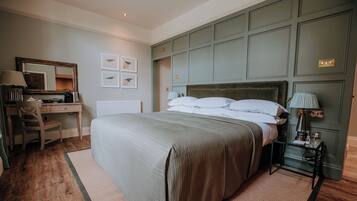 A bedroom with a large bed, a desk with a chair, a dresser, and a nightstand with a lamp.
