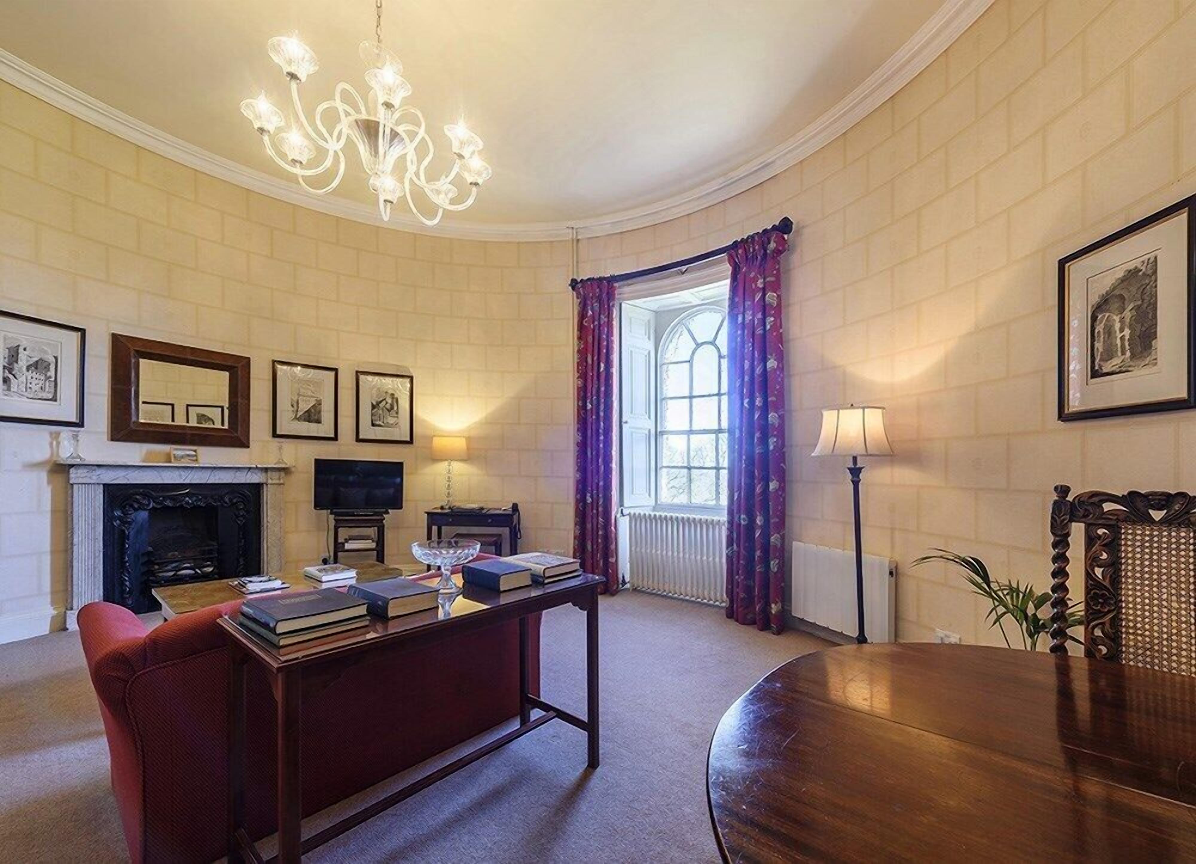 A room with a fireplace, a television, a dining table, and a chandelier.