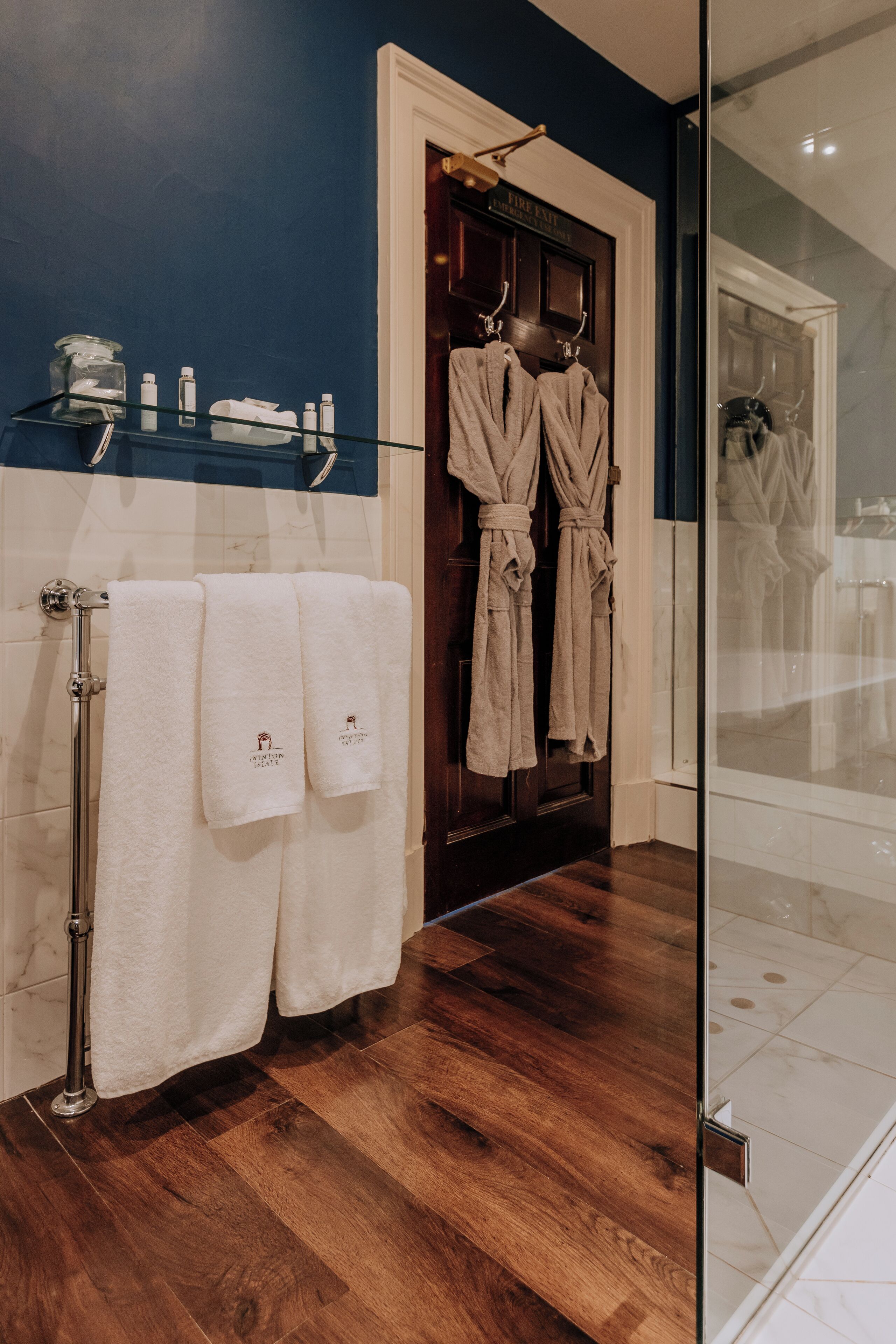 A bathroom with wooden flooring, a glass shower enclosure, and two white towels hanging on a rack.