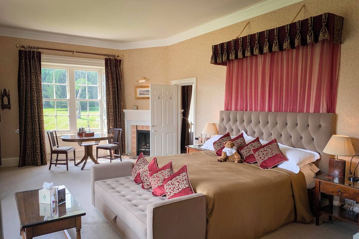 A bedroom with a large bed, a sofa, a small table, and a fireplace.