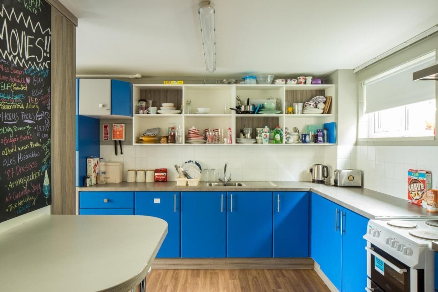 A modern kitchen with blue cabinets, white countertops, and a chalkboard wall with various writings.