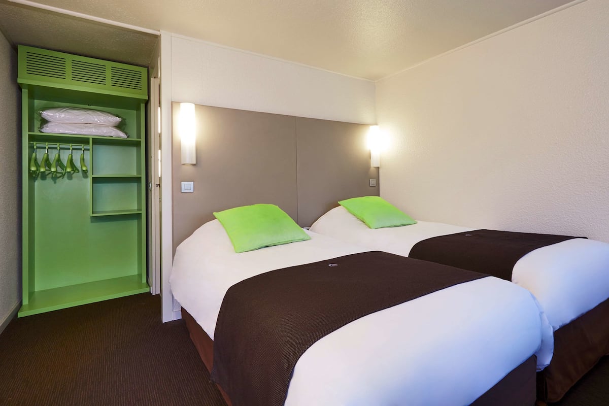 Habitación de hotel con dos camas, un armario verde y una lámpara fijada a la pared.