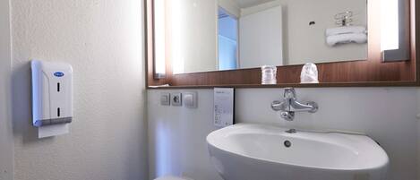 Un bagno con un lavandino bianco, uno specchio, un erogatore di sapone e un water.