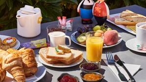 Una mesa de desayuno con croissants, tostadas, fruta y una cafetera.