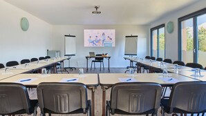 A conference room with long tables, chairs, a projector screen, and a presentation on the wall.
