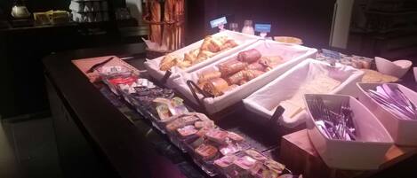 A breakfast buffet with various pastries, sandwiches, and beverages.