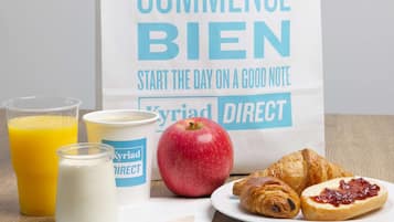 A breakfast setup with a bag, apple, croissants, and drinks on a wooden table.