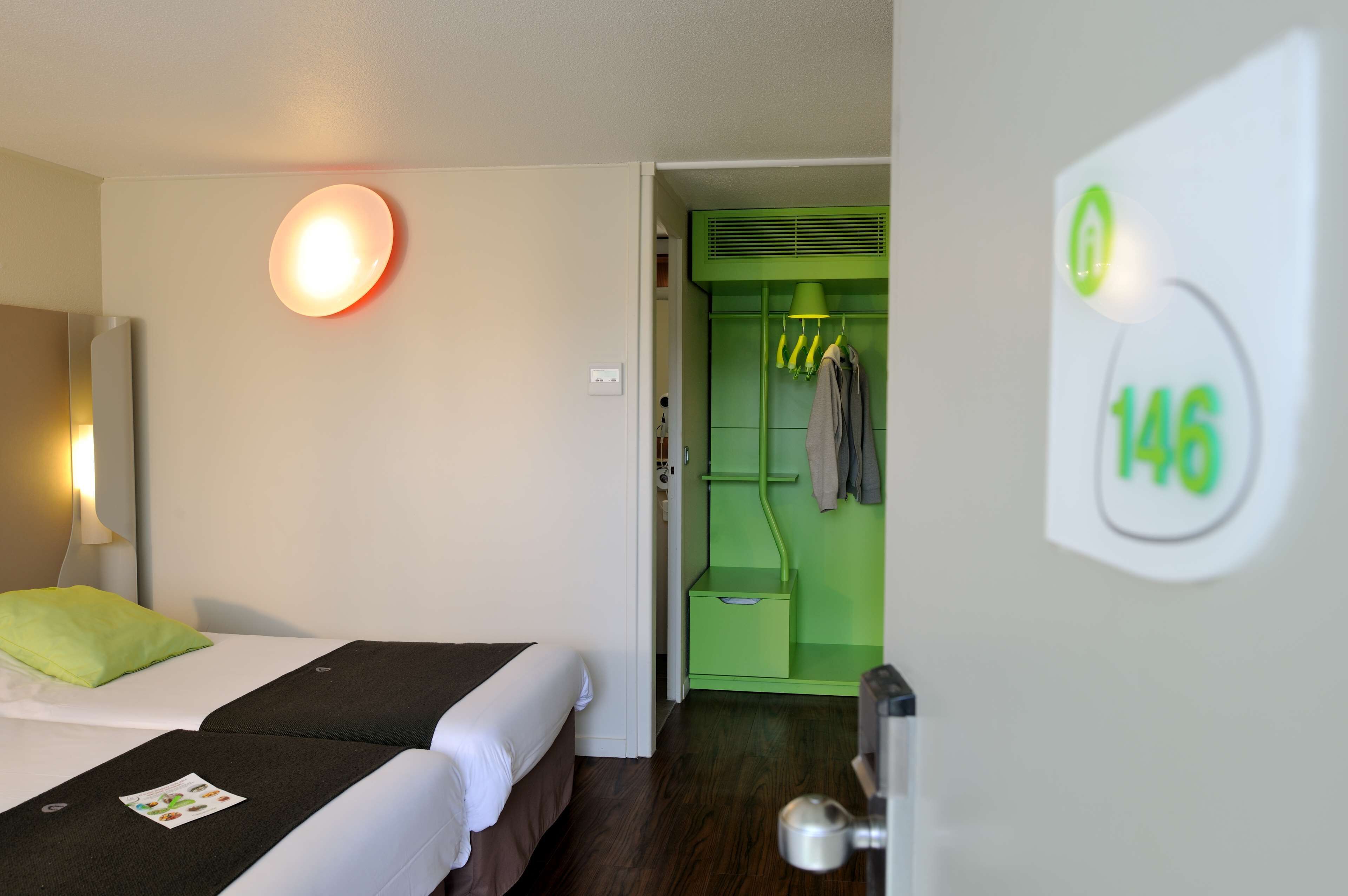 A hotel room with a bed, a green closet, and a wall-mounted light.