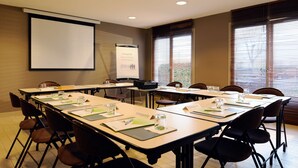 Un salón de conferencias con pantalla de proyector, pizarra para presentaciones y mesas con sillas.