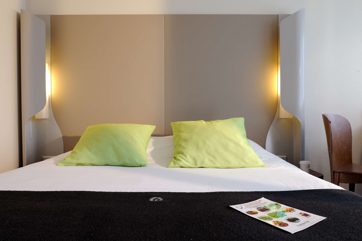 Una cama bien hecha con dos almohadas, una manta negra y un folleto sobre la cama.
