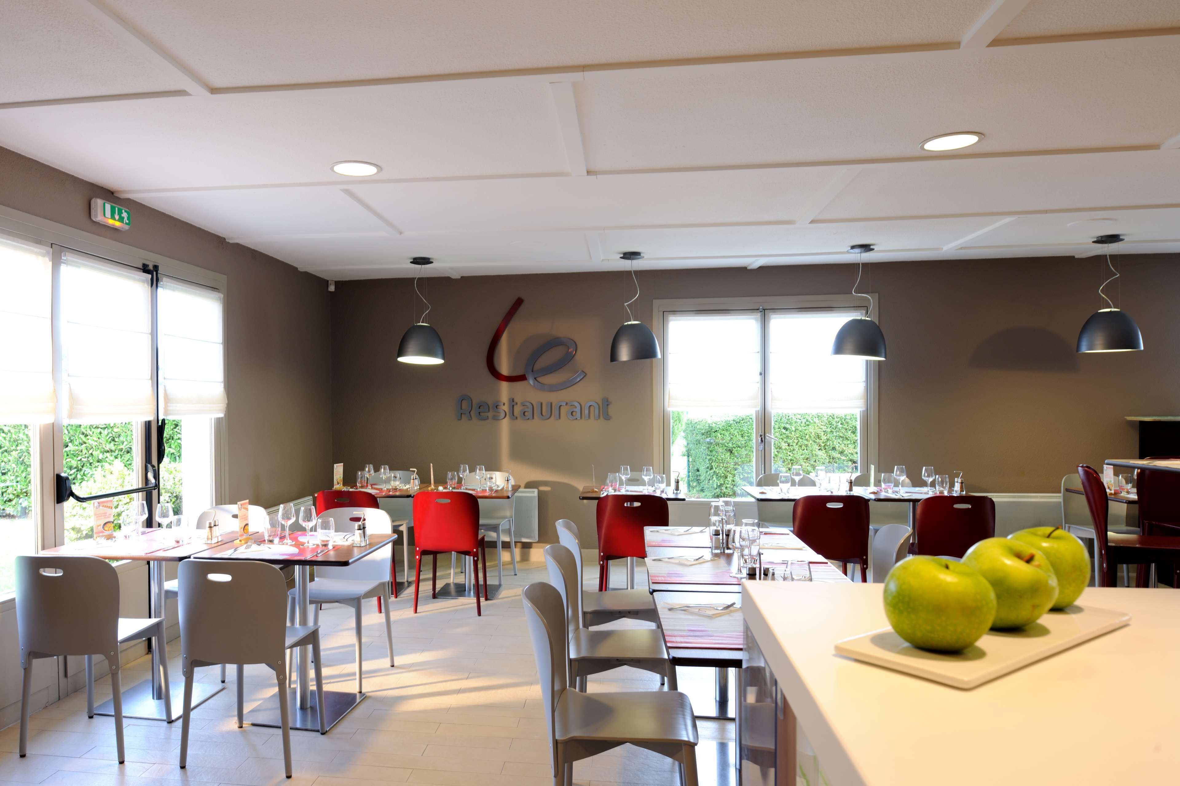 A restaurant with tables set for dining, chairs, and hanging pendant lights.