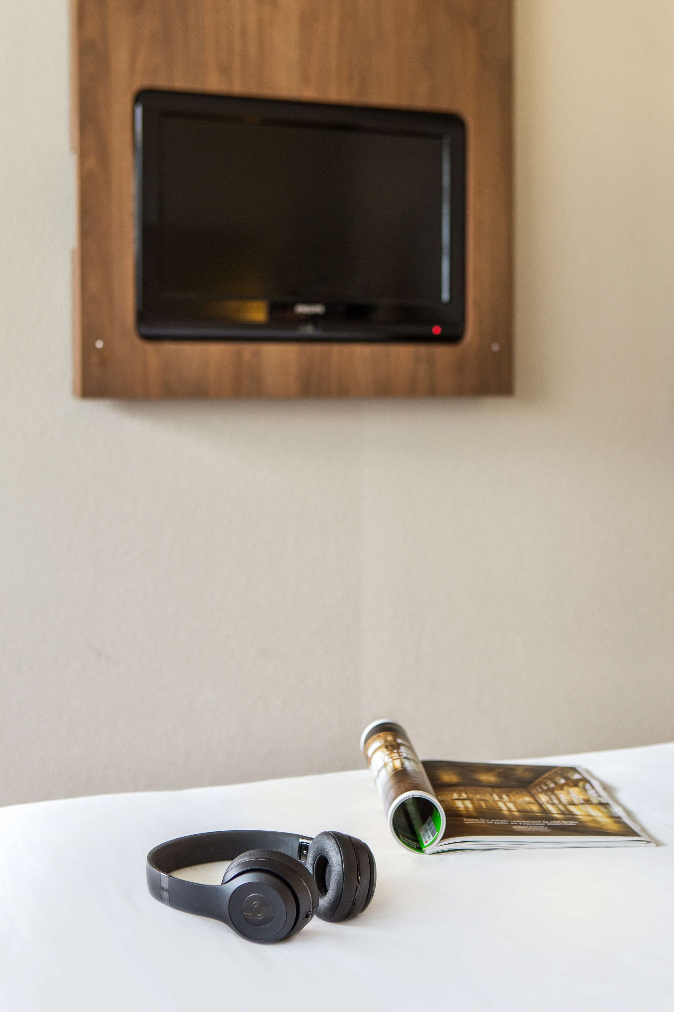 A pair of headphones on a table, a rolled-up magazine, and a television mounted on a wooden wall.