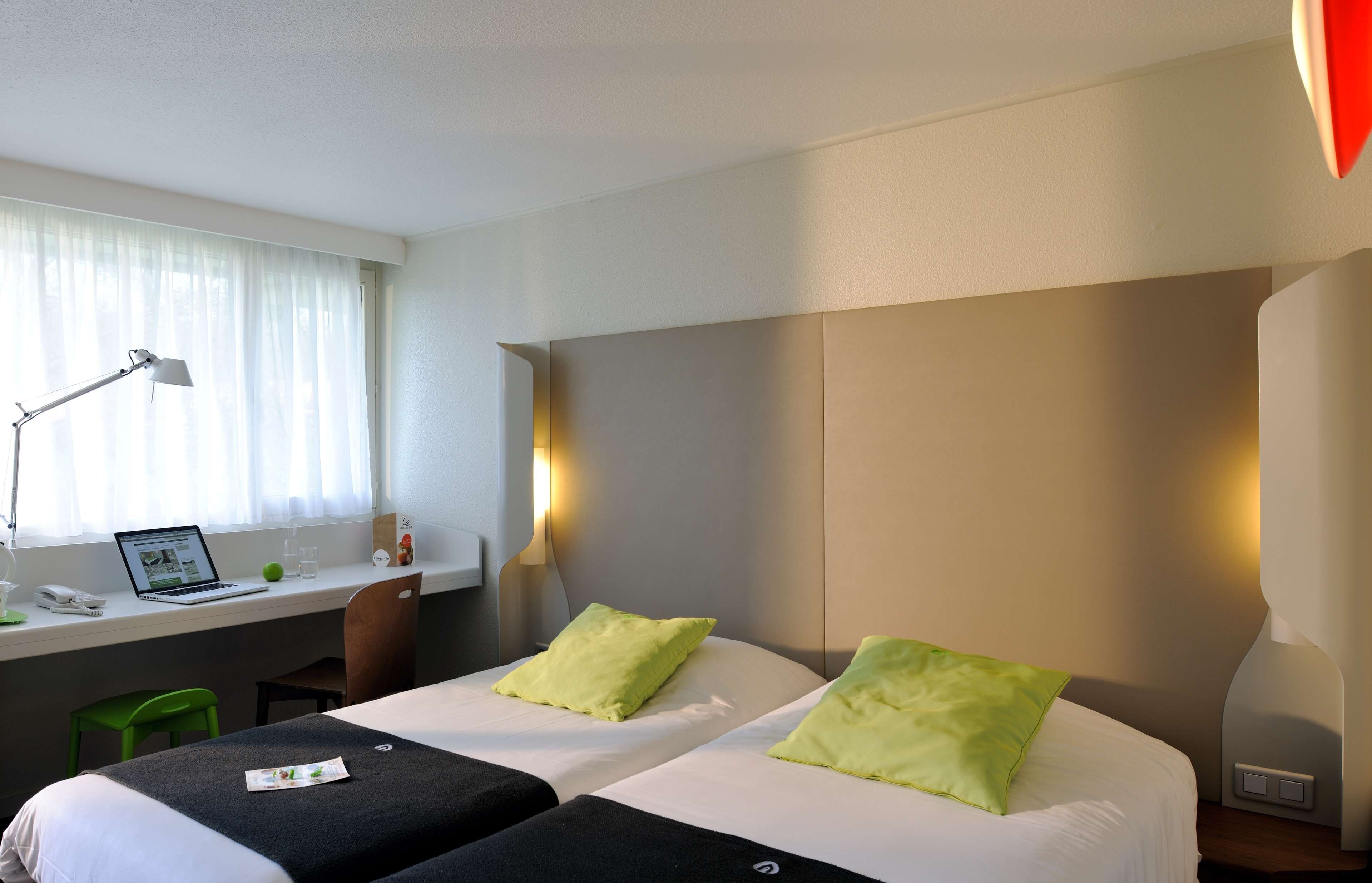 A hotel room with two beds, a desk with a laptop, a chair, and a window with curtains.