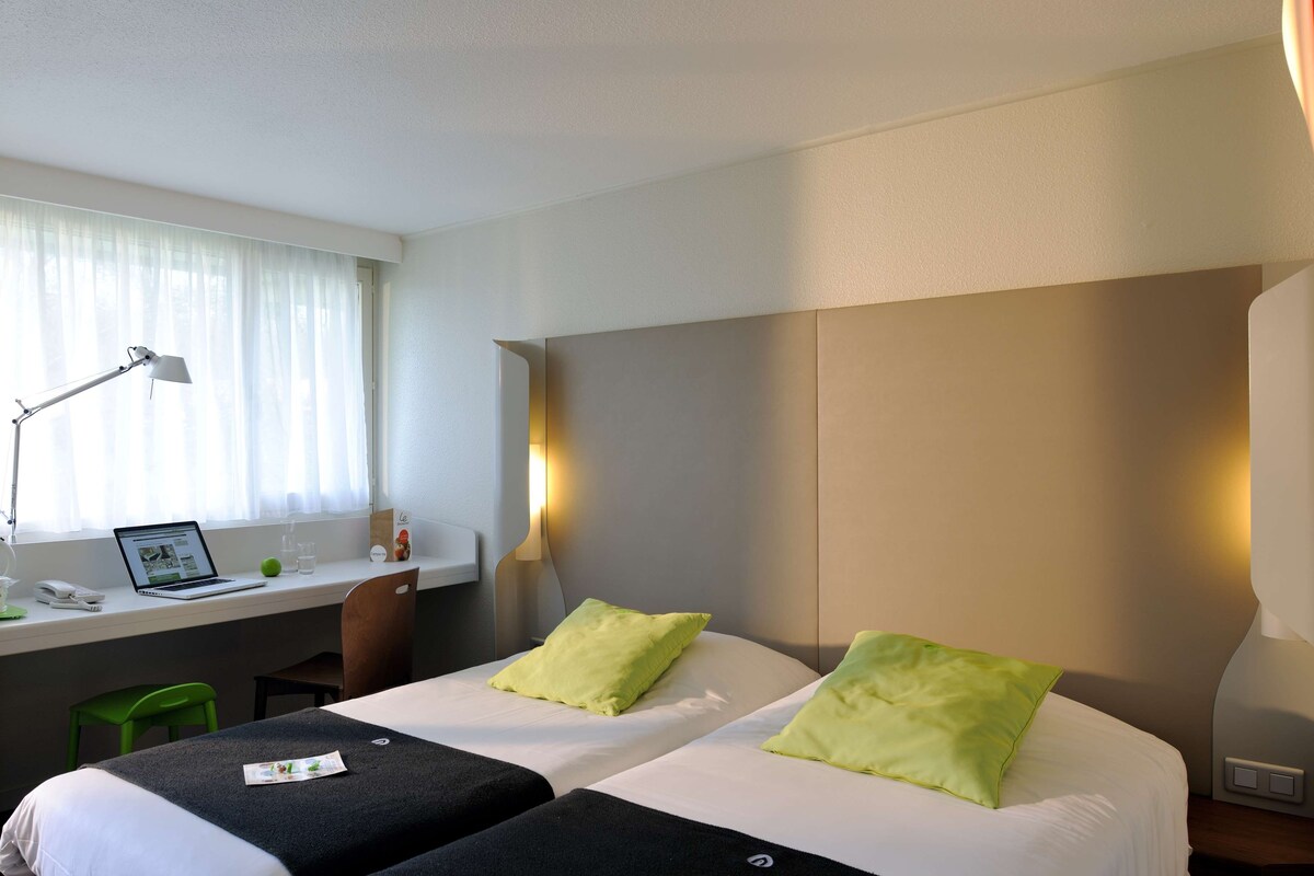 Habitación de hotel con dos camas, un escritorio, una laptop, una silla y una lámpara.