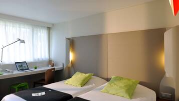 A hotel room with two beds, a desk with a laptop, a chair, and a window with curtains.