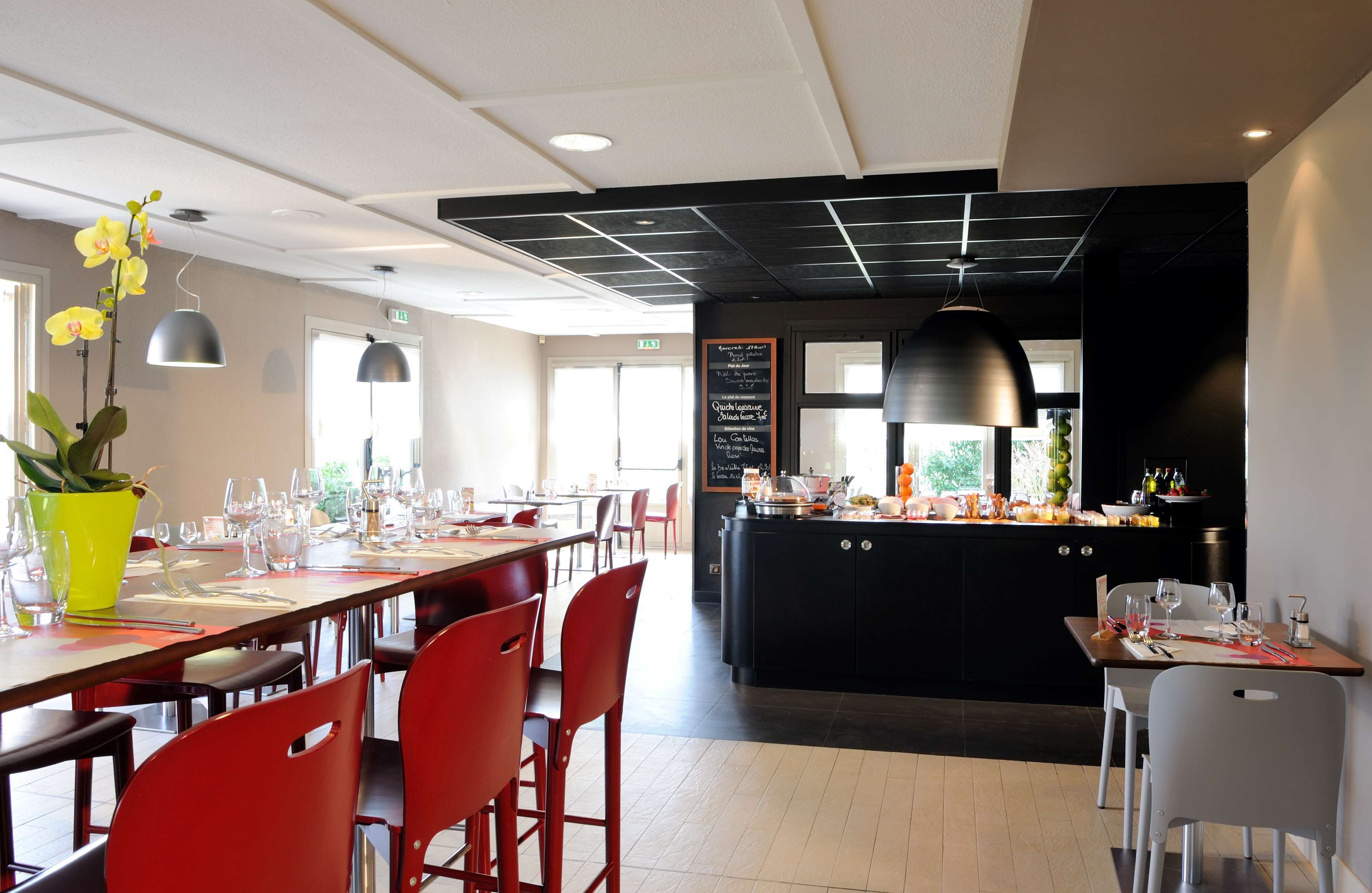 Un restaurante moderno con una larga mesa de comedor, sillas rojas y una isla central con encimera negra.