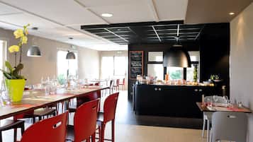 Un restaurante moderno con una larga mesa de comedor, sillas rojas y una isla central con encimera negra.