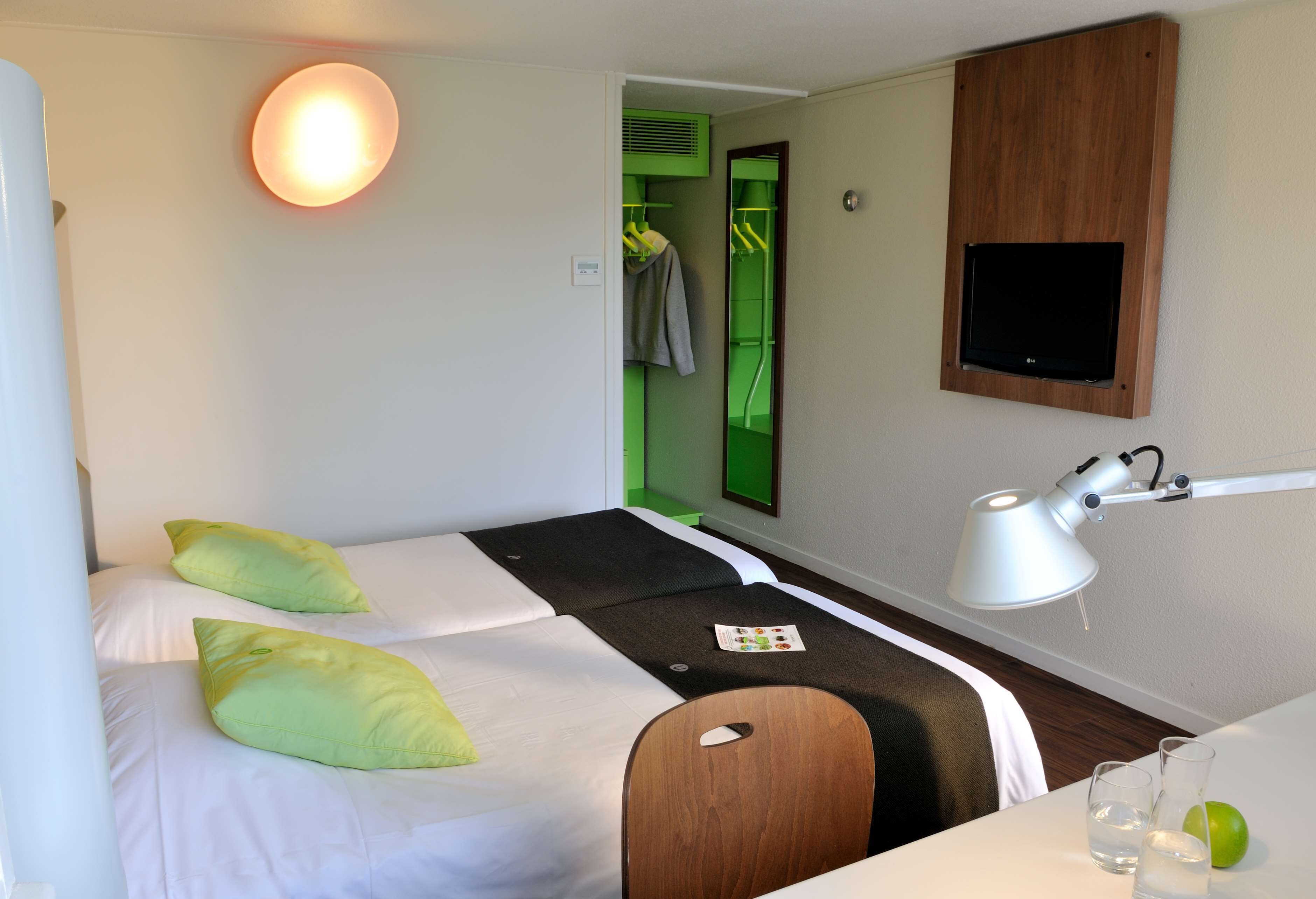 A hotel room with a bed, a desk, a mirror, a lamp, and a TV.