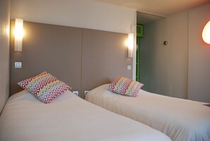 A hotel room with two beds, each with a patterned pillow, and wall-mounted lights. - Campanile Creil - Villers Saint Paul (Villers-Saint-Paul)