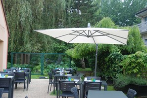An outdoor patio area with tables and chairs, surrounded by lush greenery and trees. - Campanile Creil - Villers Saint Paul (Villers-Saint-Paul)