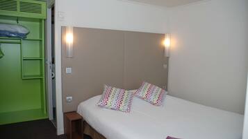 Una cama individual con dos almohadas, una mesita de noche, un armario verde y dos luces fijadas a la pared.