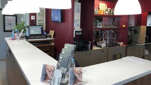 Un mostrador de recepción con una computadora, una planta y material promocional. Dos lámparas colgantes iluminan el mostrador.