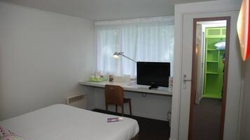 Quarto de hotel com cama, escrivaninha, cadeira e computador.