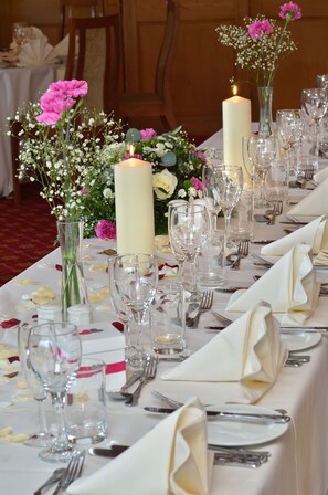 Una larga mesa dispuesta para un evento formal, con velas, copas y centros de mesa florales.