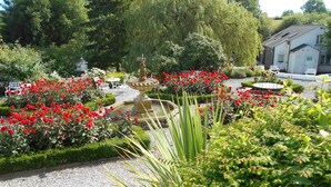 A garden with a fountain, red flowers, and a building with outdoor seating. - Damson Dene Hotel (Kendal)