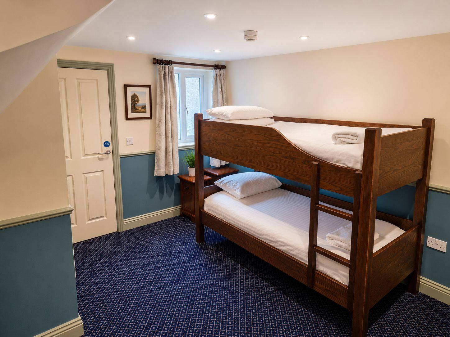 A bunk bed in a room with a patterned carpet, a window with curtains, and a door with a sign.