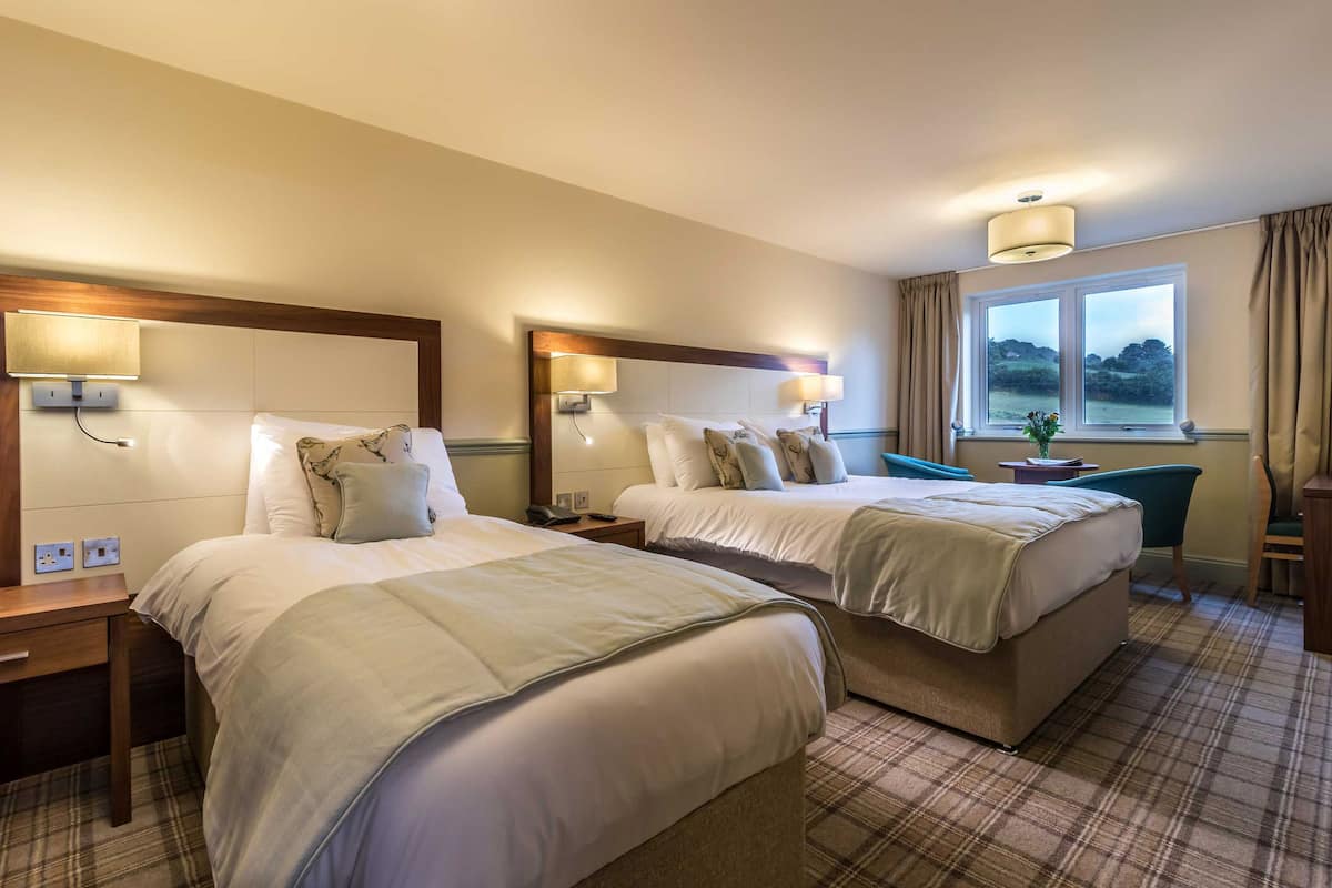 A hotel room with two beds, a desk, and a window with curtains.