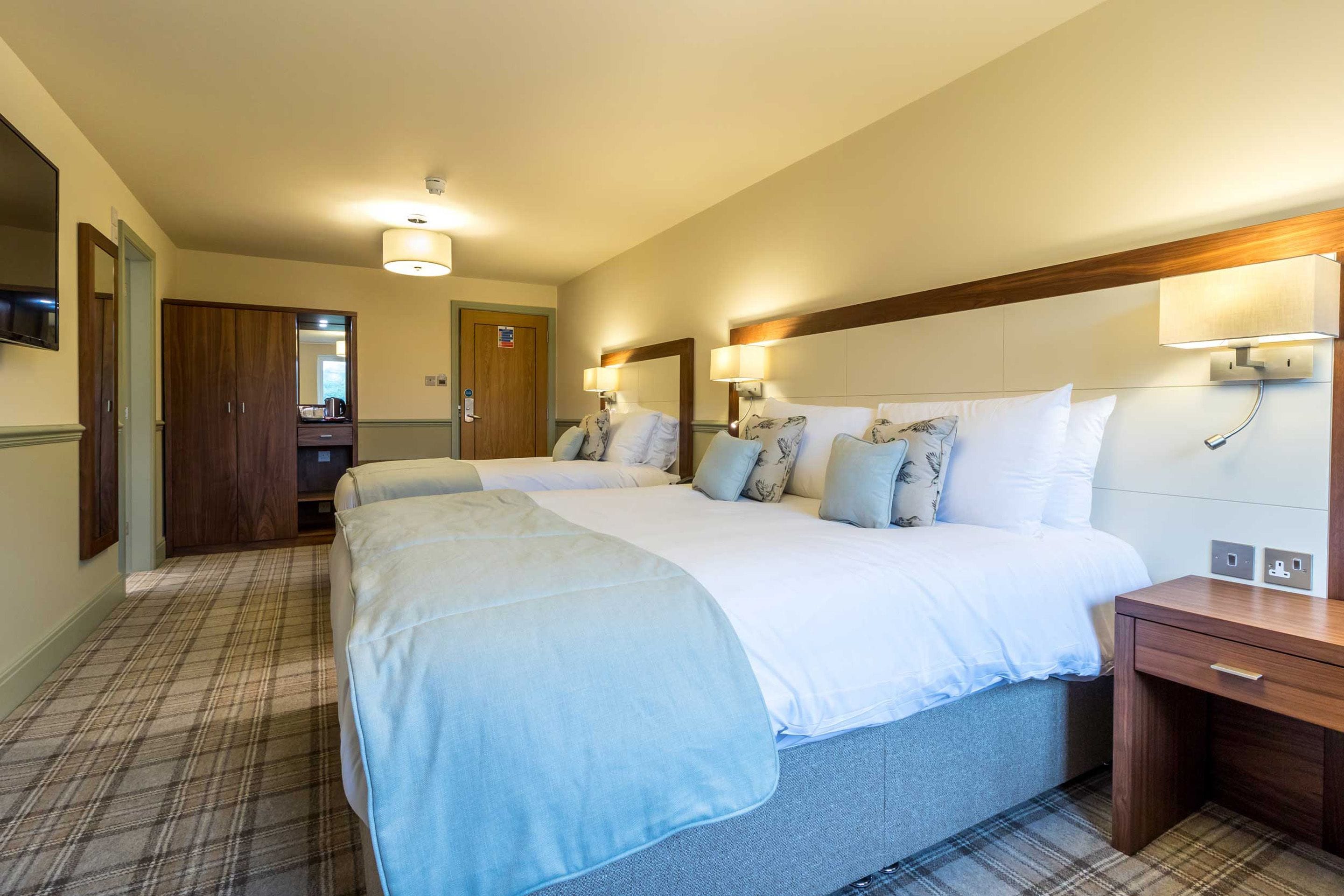 Ein Hotelzimmer mit zwei Betten, einem Holzkopfteil, einem Nachttisch und einem Spiegel.