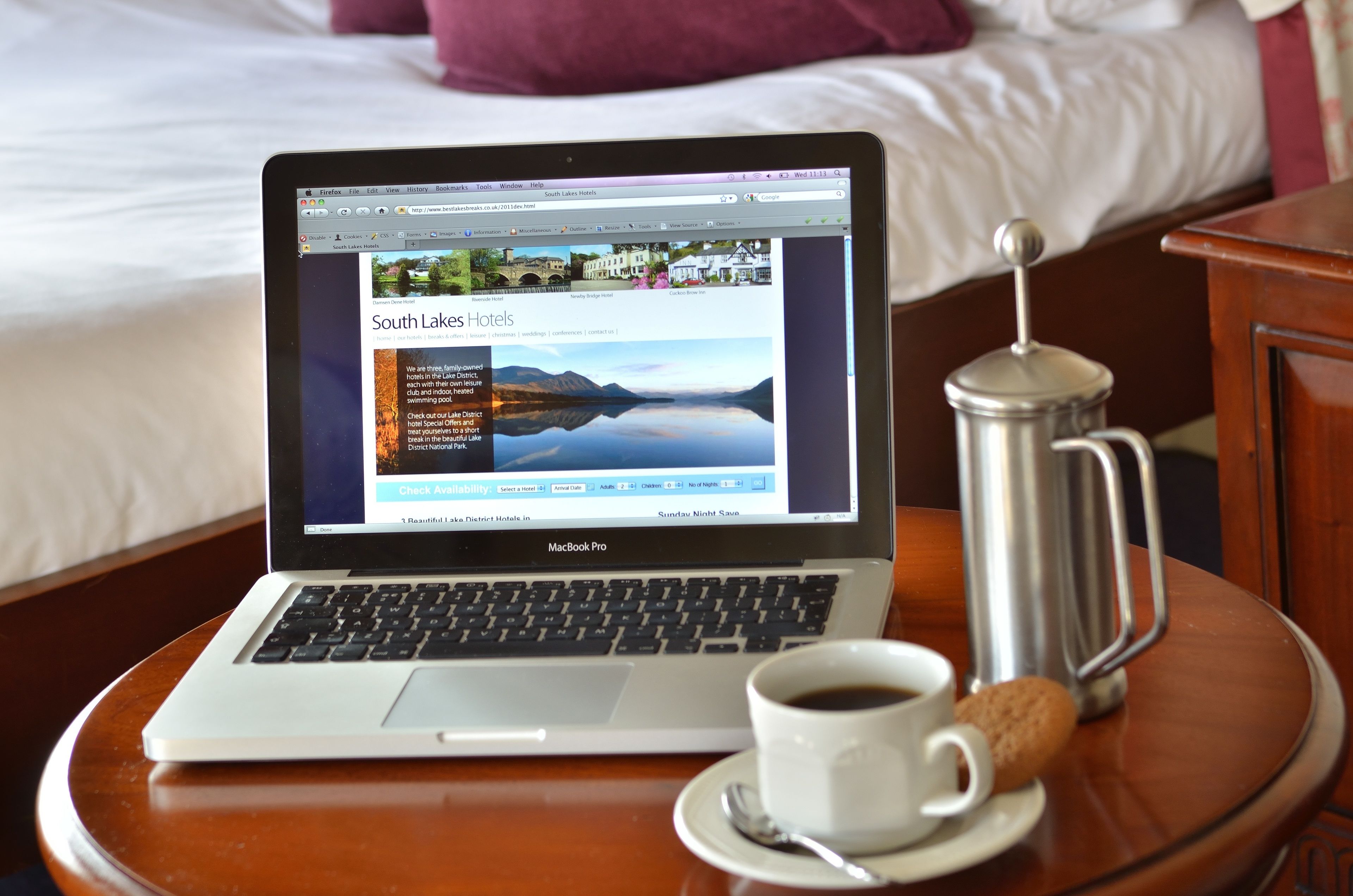 A MacBook Pro on a wooden table with a cup of coffee and a sugar packet beside it.