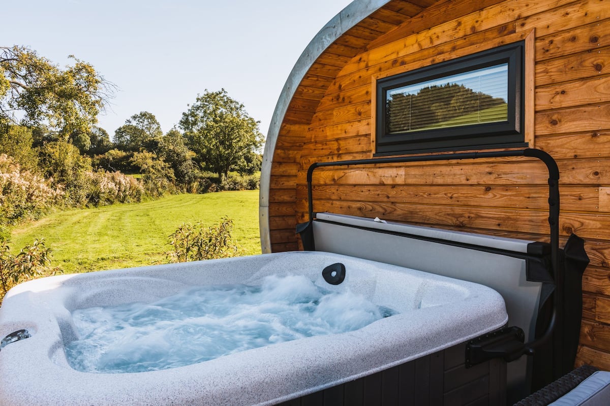 A hot tub in a wooden cabin with a view of a grassy field and trees.