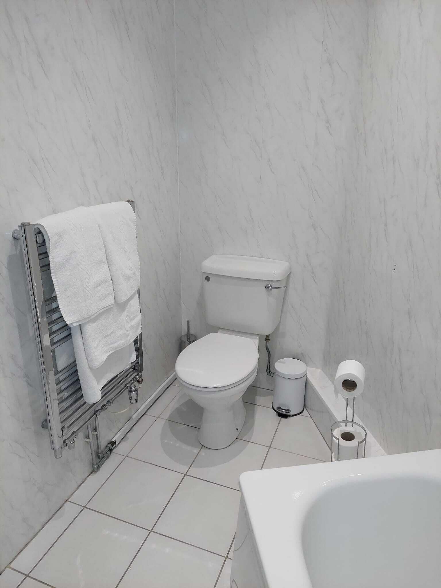 A bathroom with a toilet, a towel rack with towels, a toilet paper holder, and a bathtub.