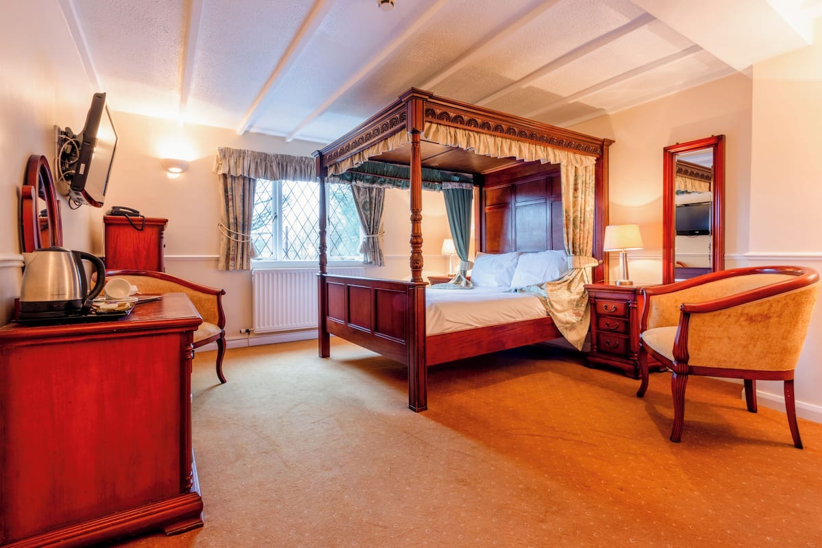 A four-poster bed with a canopy, a wooden dresser, a chair, and a mirror on the wall.
