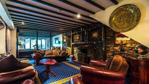 A cozy lounge area with leather sofas, a patterned rug, and a stone fireplace. - Damson Dene Hotel (Kendal)
