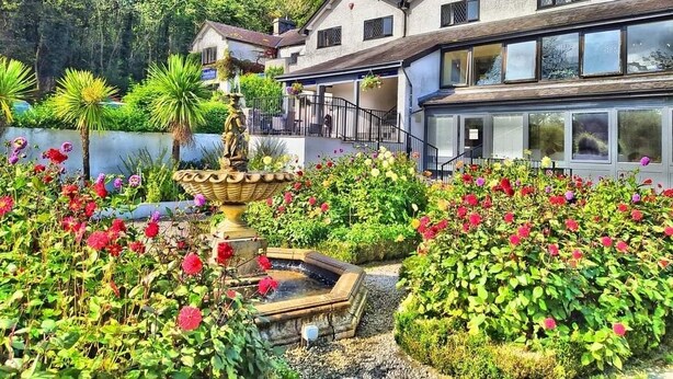 A two-story house with a garden in front, a pond, and a fountain. - Damson Dene Hotel (Kendal)