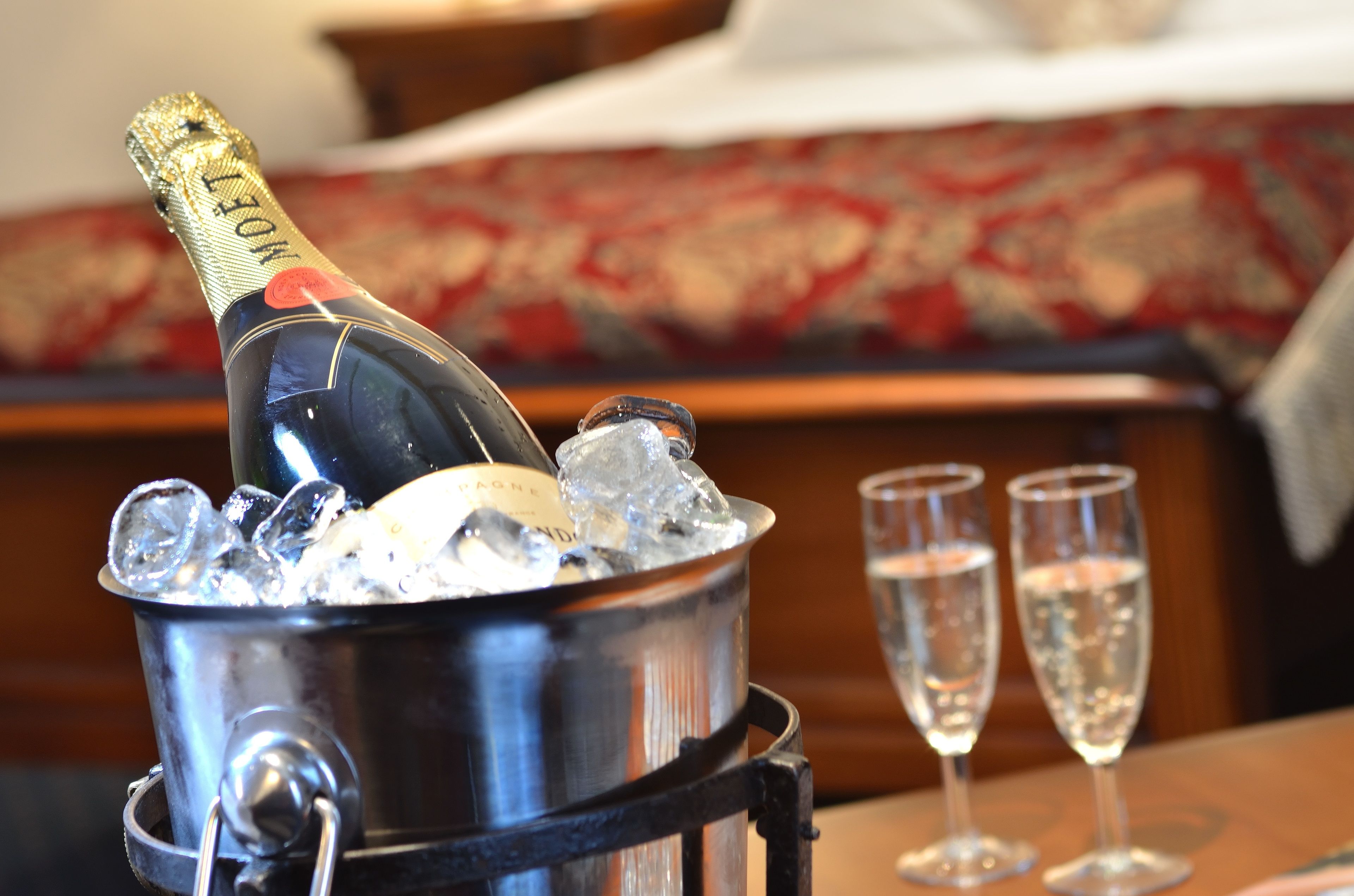 A bottle of champagne in an ice bucket with two glasses beside it.