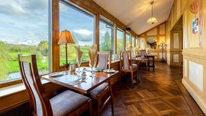 A dining area with wooden furniture, large windows, and a view of a green landscape. - Damson Dene Hotel (Kendal)