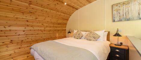 Ein Schlafzimmer mit Holzbalkendecke, einem Bett mit weißer Bettwäsche, einem Nachttisch mit Lampe und einem Bild an der Wand.