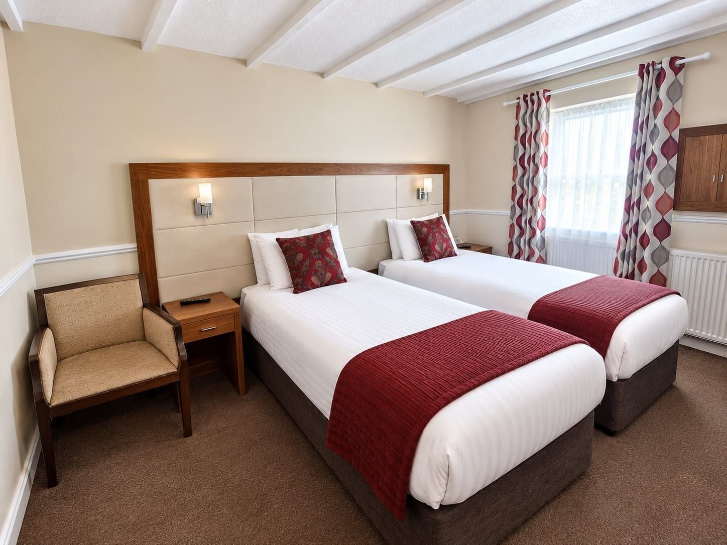 A hotel room with two beds, a chair, a nightstand, and a window with curtains.