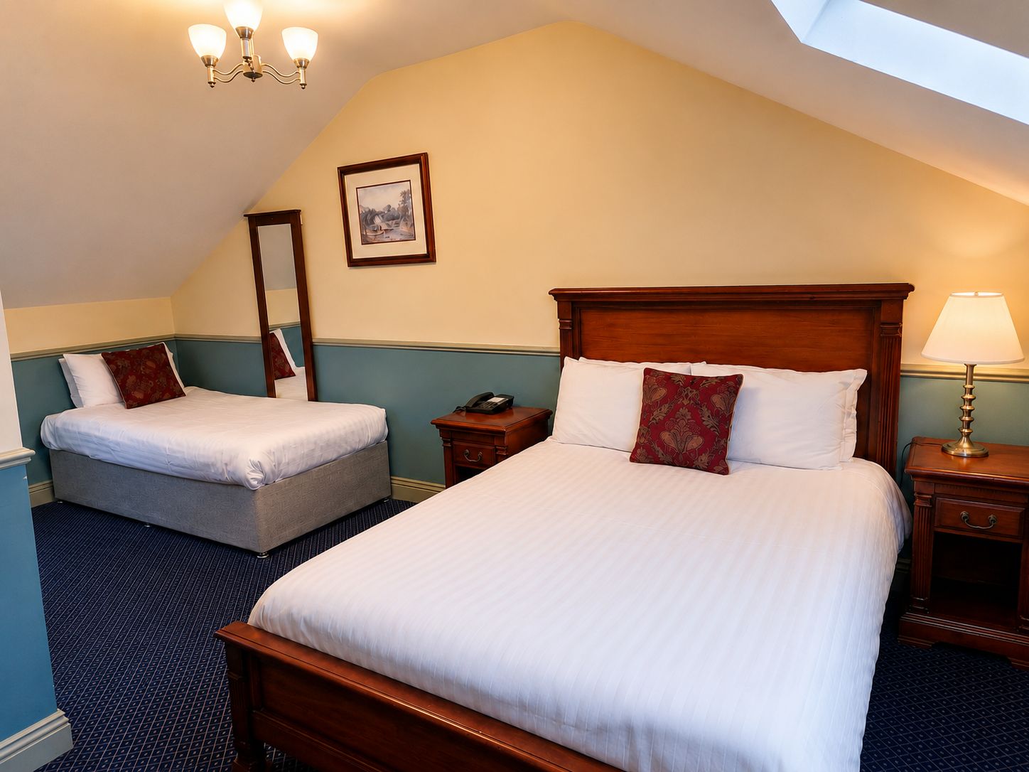 A hotel room with two beds, a wooden headboard, a bedside lamp, a telephone, and a framed picture on the wall.