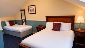 A hotel room with two beds, a wooden headboard, a bedside lamp, a telephone, and a framed picture on the wall.