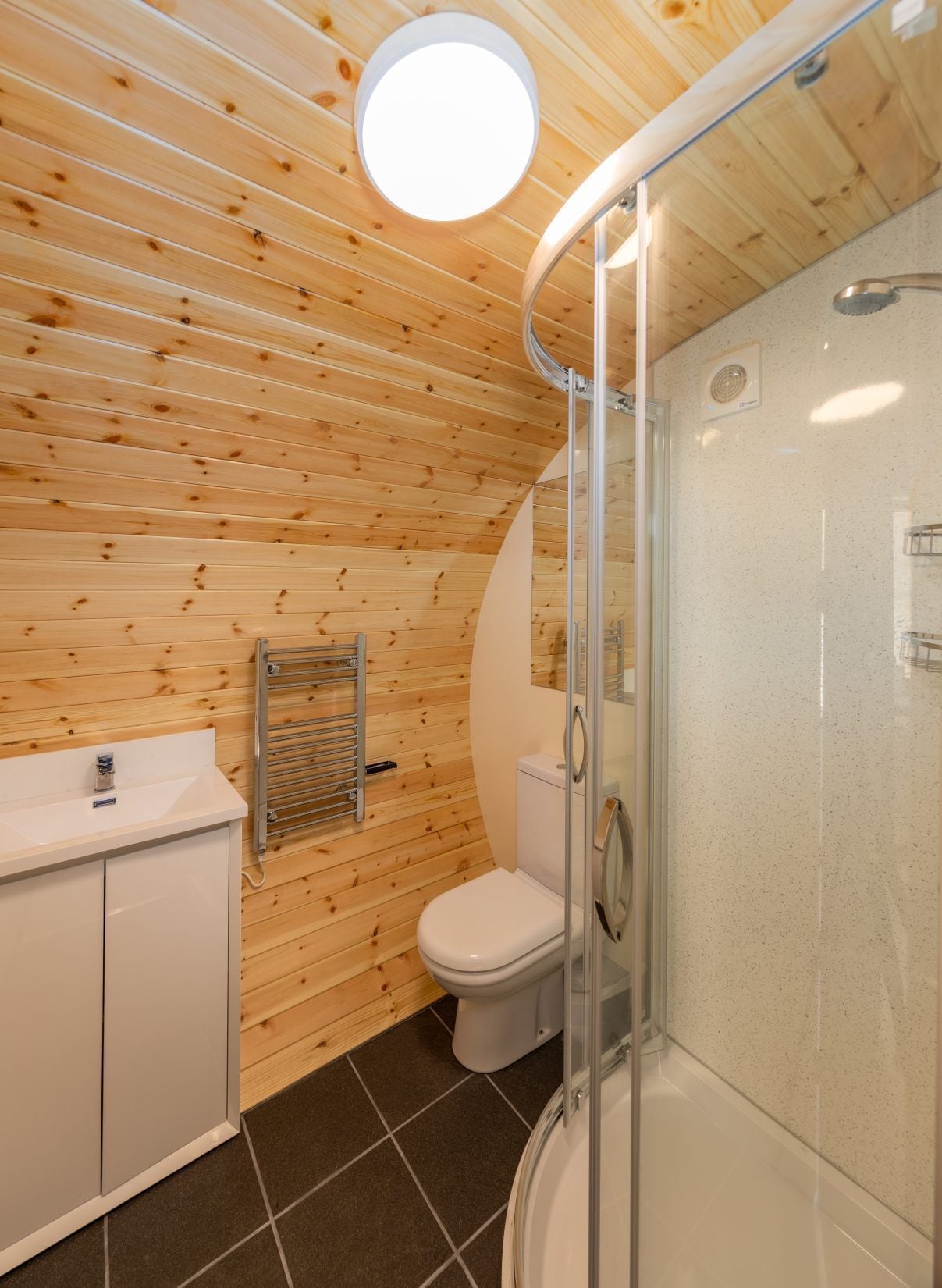 A bathroom with wooden walls, a glass shower enclosure, a white sink, and a toilet.